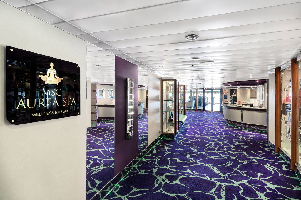 Eingangsbereich des Aurea Spa mit beleuchteter Beschilderung und lila Designteppich auf einem Kreuzfahrtschiff