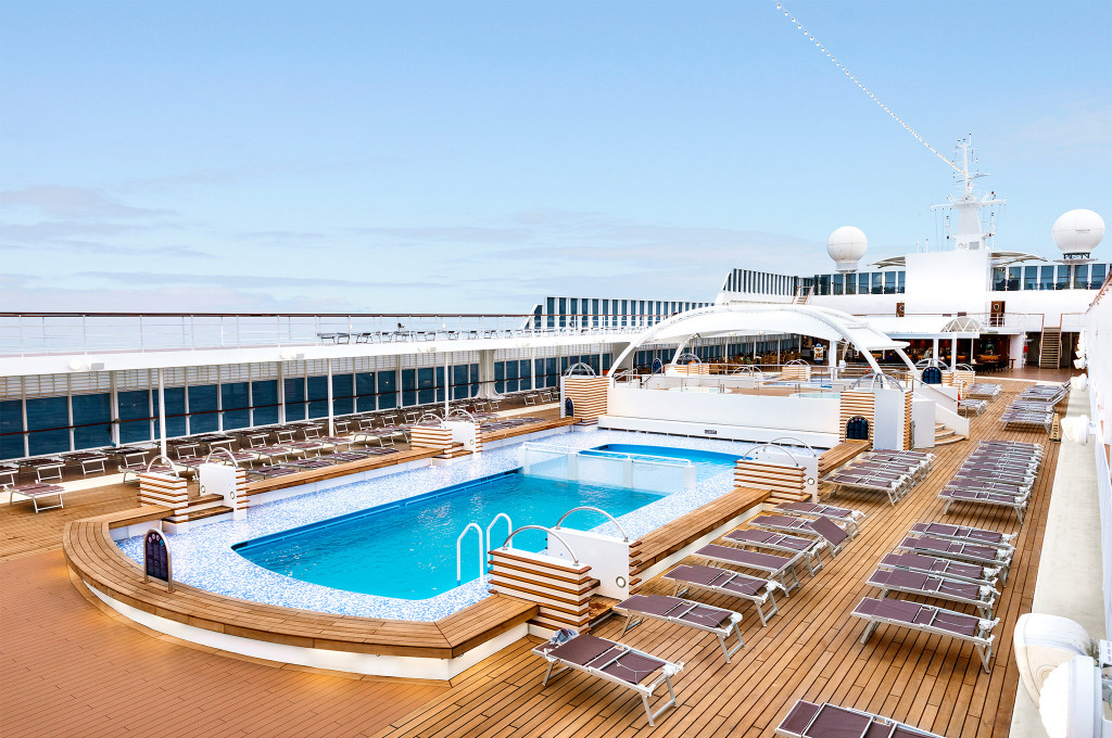 Großer Außenpool mit Liegestühlen und Holzdeck auf dem Sonnendeck eines Kreuzfahrtschiffes
