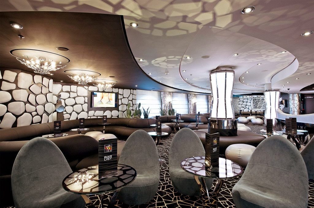 Moderne Bar mit grauen Schalensesseln, dunklen Sofas und organischer Steinmosaik-Wandverkleidung