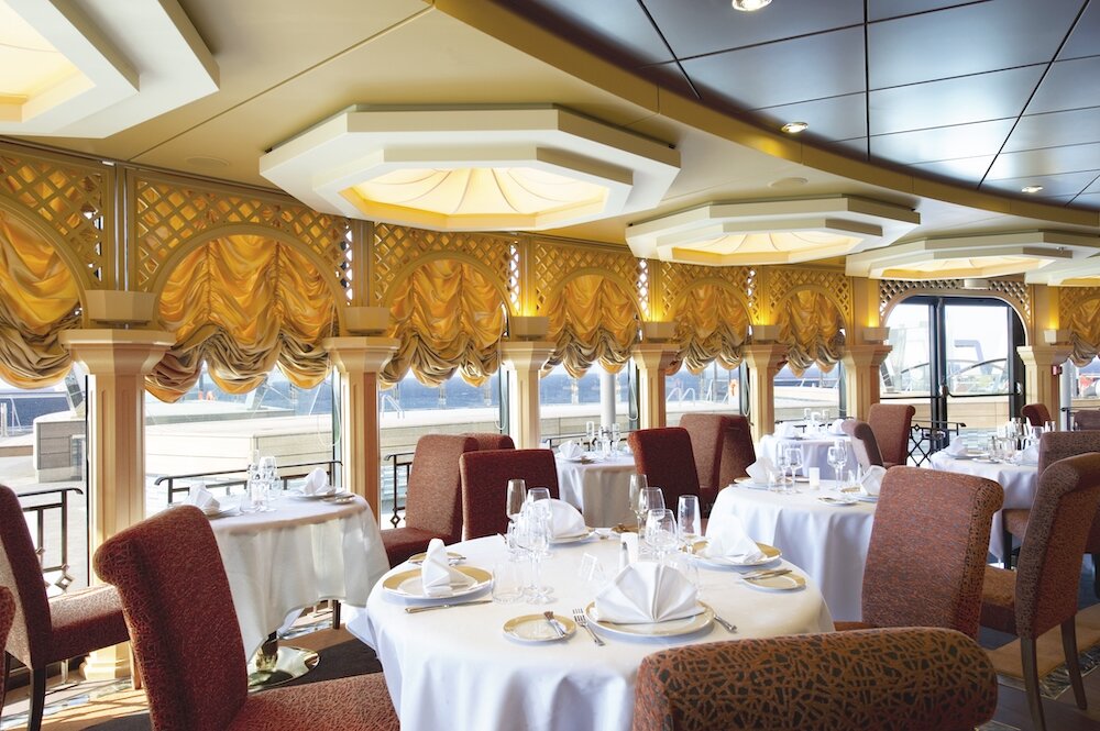 Elegantes Restaurant mit goldenen Raffvorhängen, kassettierten Deckenleuchten, dunkelroten Sesseln und weißen Tischdecken
