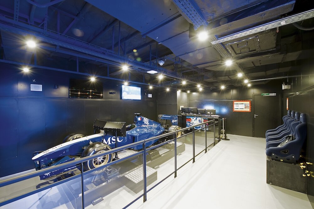 F1-Simulator auf der MSC Divina mit blauem MSC-Rennwagen auf Plattform und Zuschauerbereich