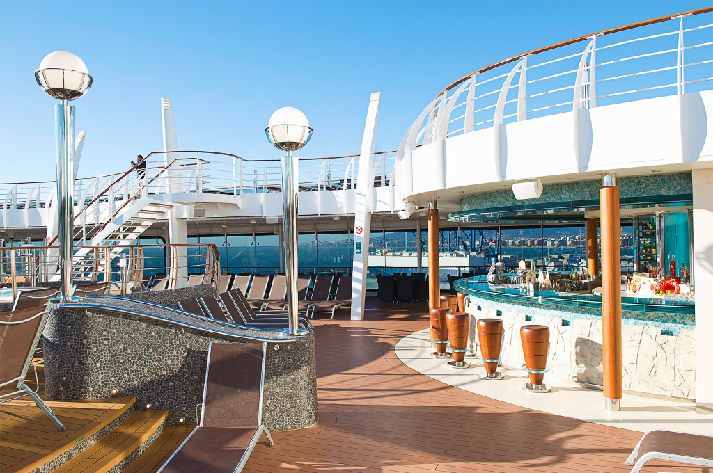 Sonnendeck mit Whirlpool, Liegestühlen und Poolbar im Hintergrund mit Blick auf einen Hafen