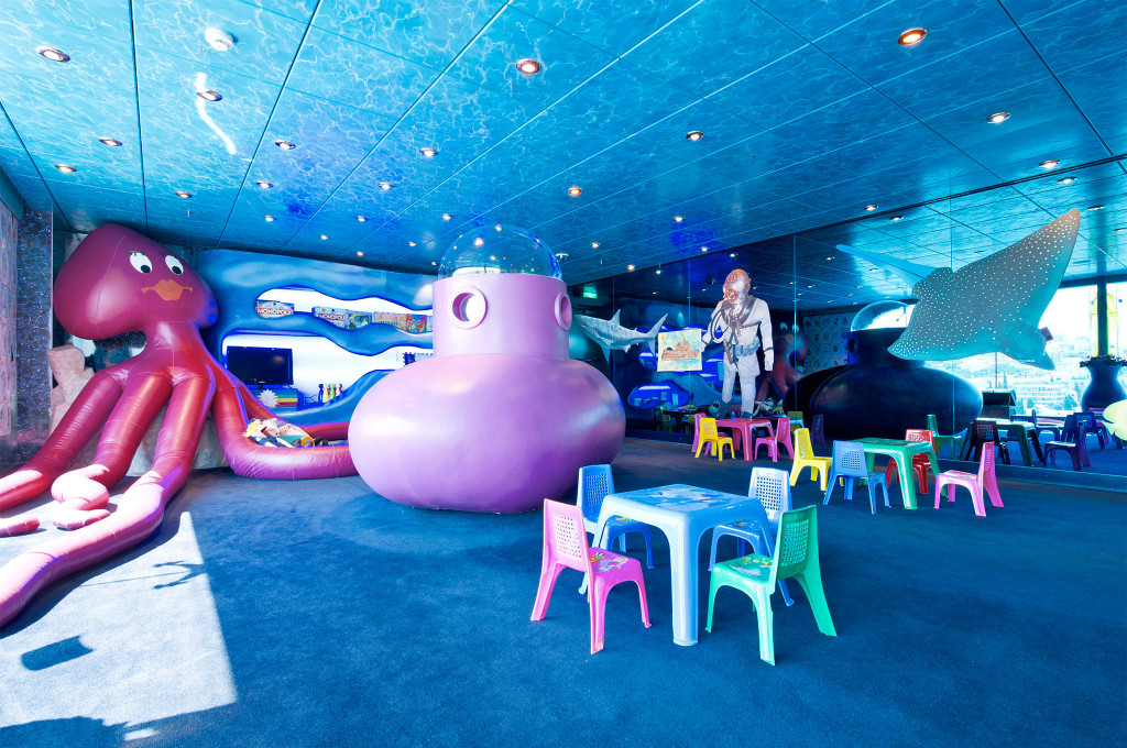 Unterwasser-Kinderspielraum mit riesigem aufblasbaren Tintenfisch, lila U-Boot-Figur, Mantarochen-Deko und bunten Kinderstühlen auf einem Kreuzfahrtschiff