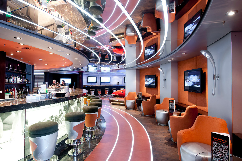 Sportsbar mit Barkeepern am geschwungenen Tresen, orangefarbenen Sesseln, TV-Bildschirmen und Spiegeldecke auf einem Kreuzfahrtschiff