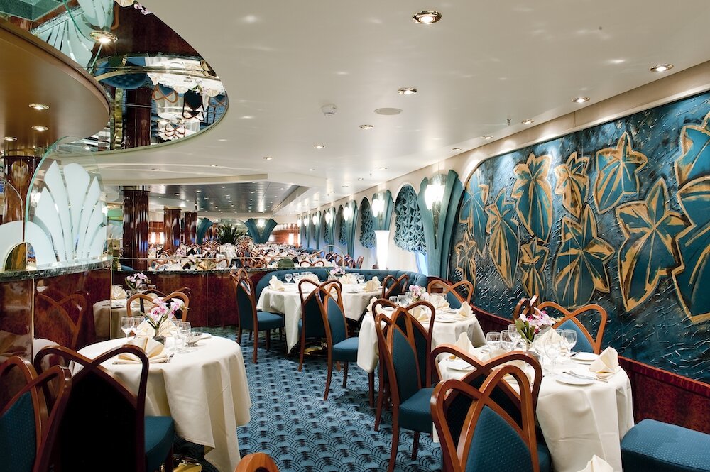 L'Edera Restaurant auf der MSC Magnifica mit kunstvollen Wandgemälden, weißen Tischdecken und klassischer Einrichtung