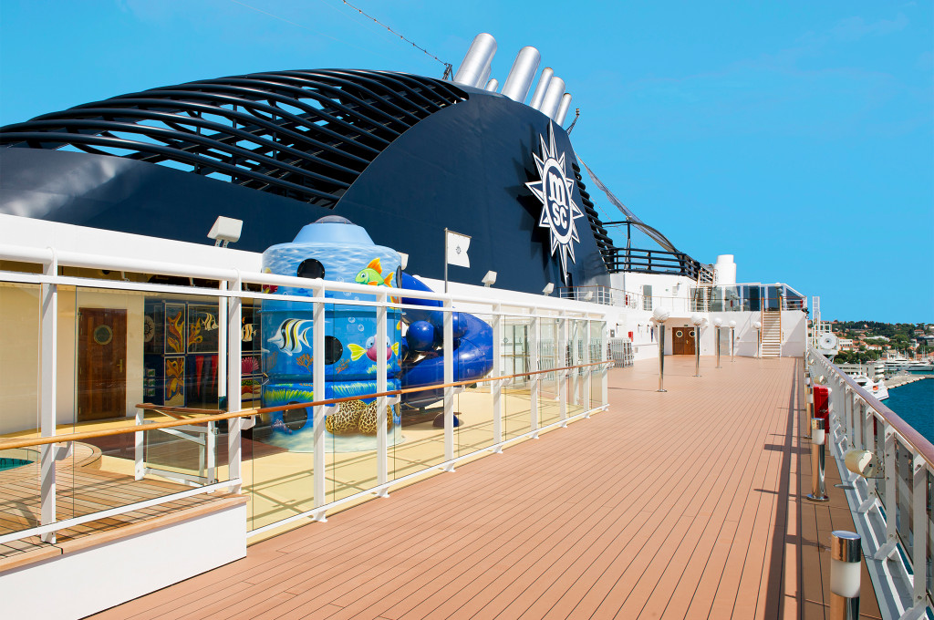 Oberdeck mit bunter Wasserrutsche und Kinderbereich mit Tropenfisch-Motiven, MSC-Schornstein und Hafenblick auf einem Kreuzfahrtschiff
