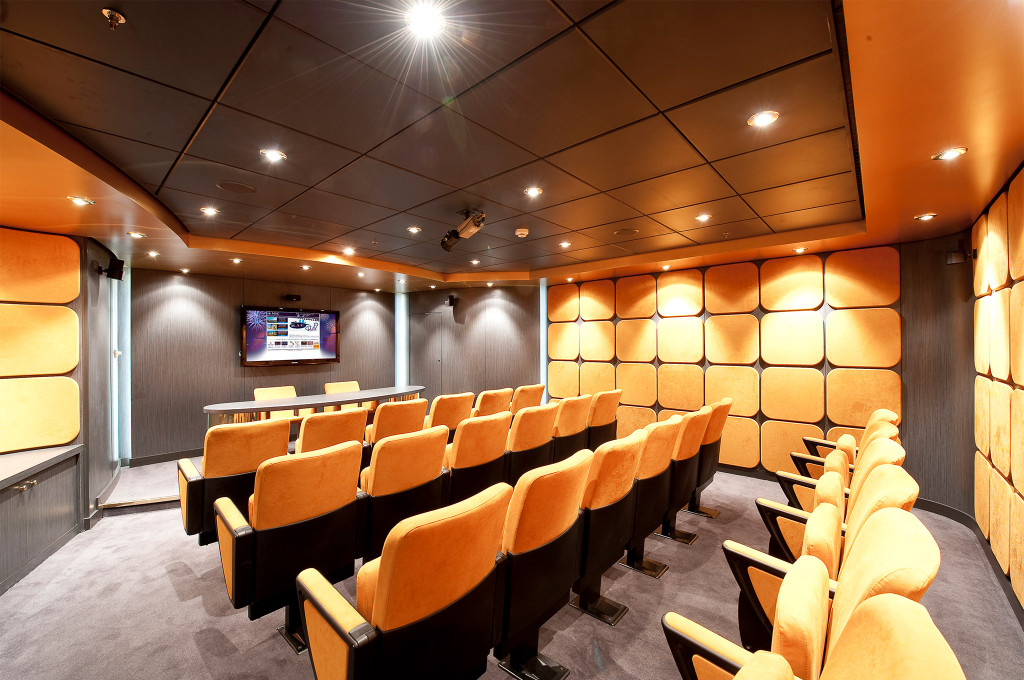 Kleiner Kinoraum mit orangefarbenen Samtsitzen, gepolsterten Wandpaneelen und Leinwand auf einem Kreuzfahrtschiff