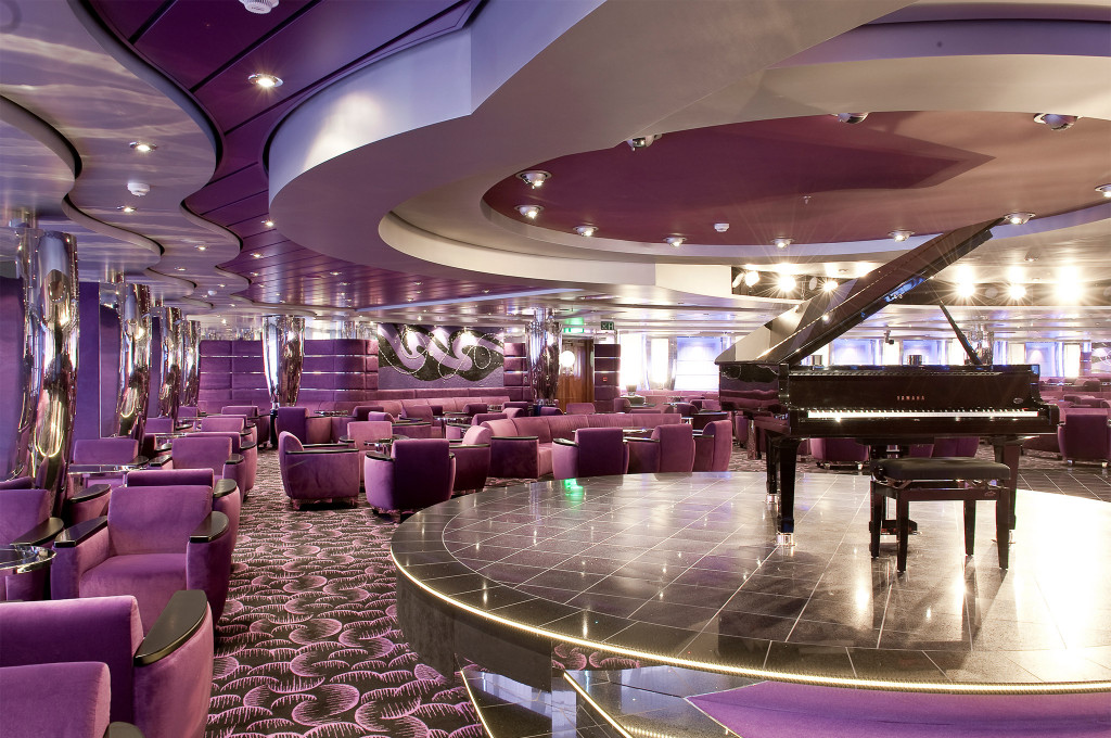 Elegante lila Lounge mit Yamaha-Flügel auf beleuchtetem Podest, lilafarbenen Samtsesseln und glänzenden Chromsäulen auf einem Kreuzfahrtschiff