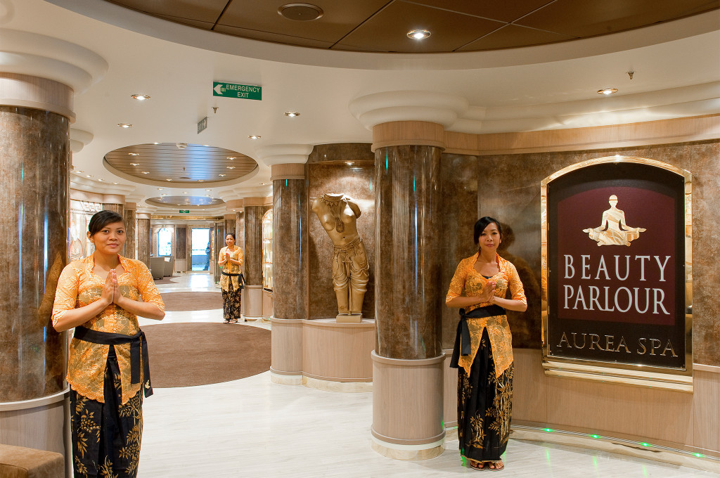 Eingangsbereich des Aurea Spa Beauty Parlours mit zwei Mitarbeiterinnen in traditioneller Tracht, Marmorsäulen und goldener Statue auf einem Kreuzfahrtschiff
