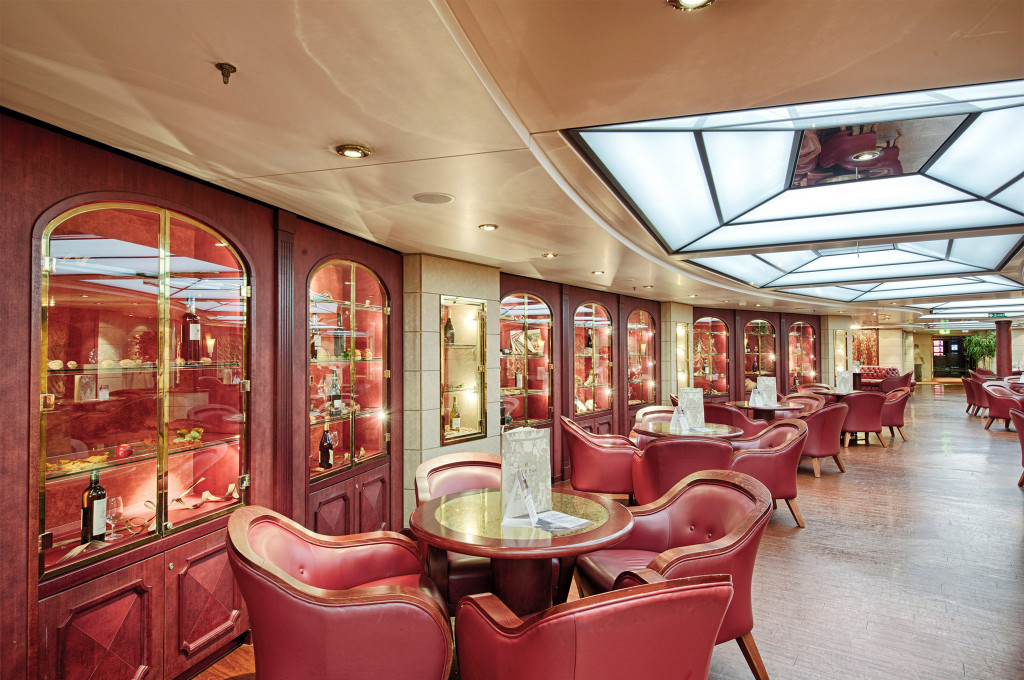 Elegante Weinbar auf einem Kreuzfahrtschiff mit dunkelroten Ledersesseln, beleuchteten Vitrinen und Weinflaschenpräsentation