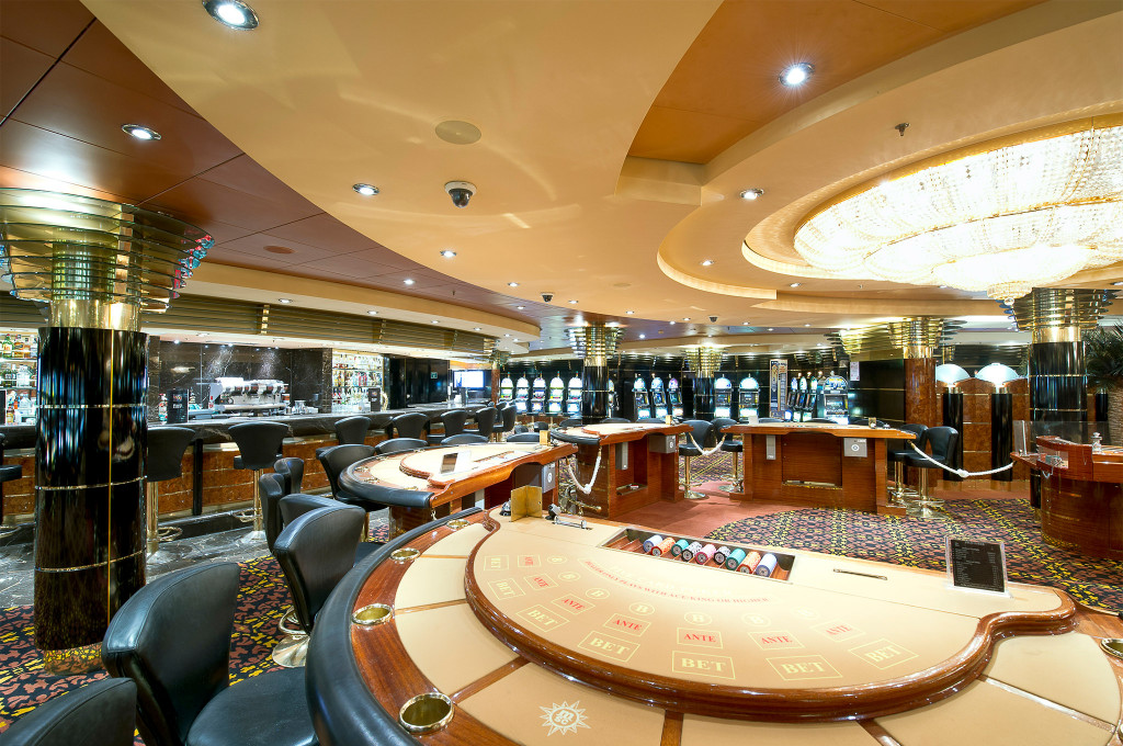 Casino auf einem Kreuzfahrtschiff mit Poker- und Blackjacktischen, Spielautomaten und großem Kristallkronleuchter