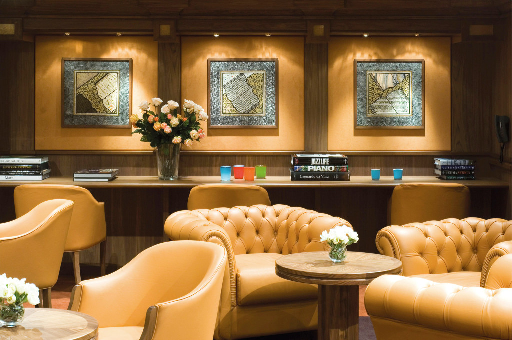 Gemütliche Bibliotheks-Lounge auf einem Kreuzfahrtschiff mit Chesterfield-Ledersofas, beleuchteten Kunstwerken und Kaffeebüchern auf einer Ablage
