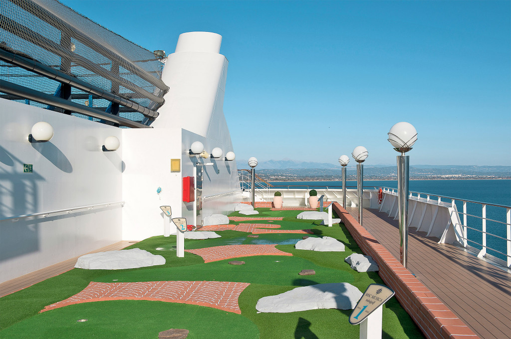 Minigolf-Anlage auf dem Außendeck eines Kreuzfahrtschiffes mit grünem Kunstrasen, Hindernissen und Meerblick