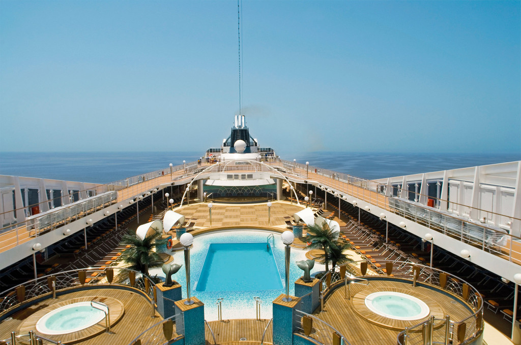Vogelperspektive des Pooldecks auf einem Kreuzfahrtschiff mit Pool, zwei Whirlpools im Vordergrund, Palmen und Liegestühlen