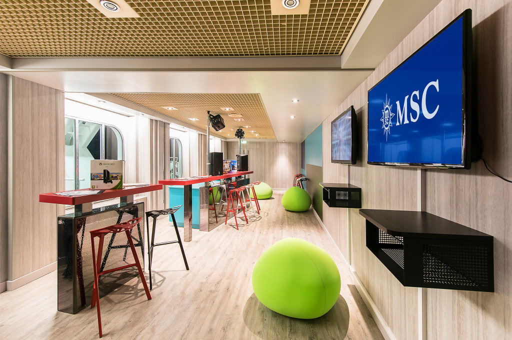 Teen Club der MSC Sinfonia mit Xbox-Spielstation, grünen Sitzsäcken, roten Stehtischen und Bildschirm