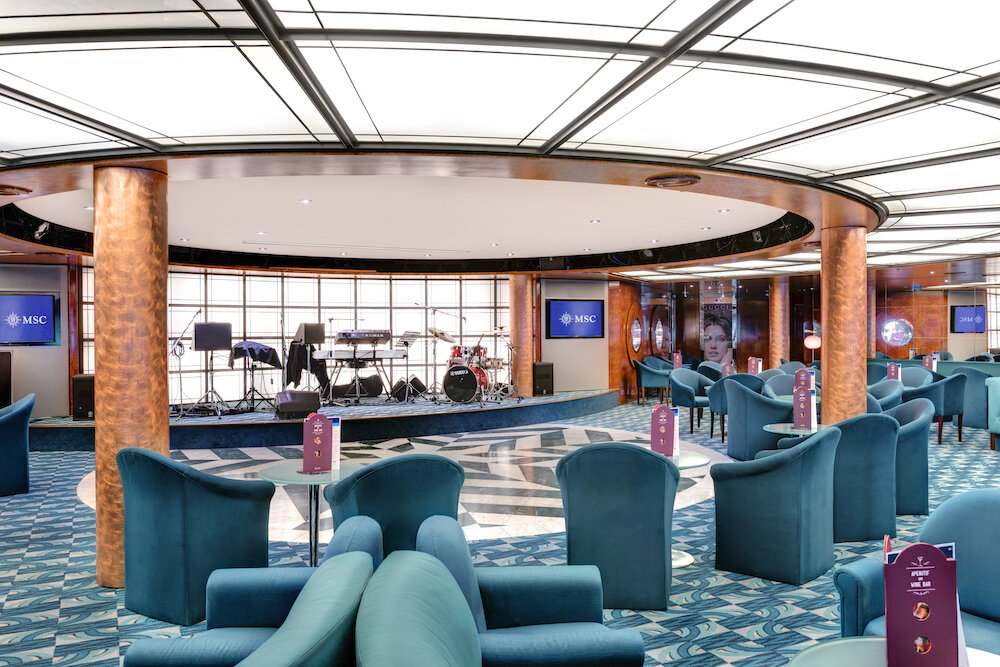 Elegante Bar-Lounge mit türkisblauen Sesseln, Musikbühne mit Schlagzeug und kreisförmiger Deckenbeleuchtung auf der MSC Sinfonia