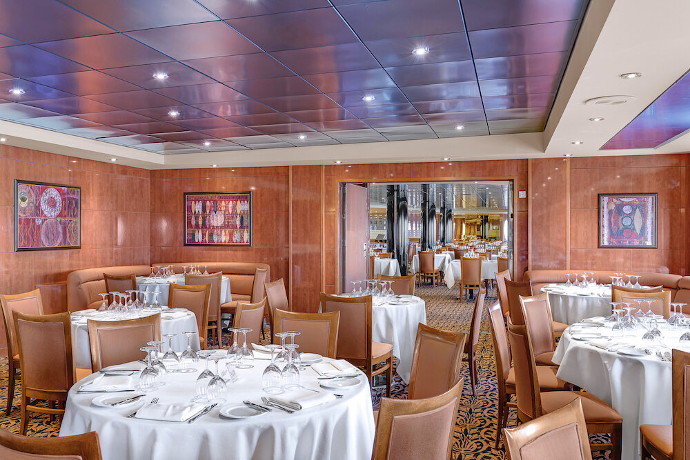 Elegantes Restaurant mit runden Tischen, weißen Tischdecken, Holzwandverkleidung und abstrakter Wandkunst