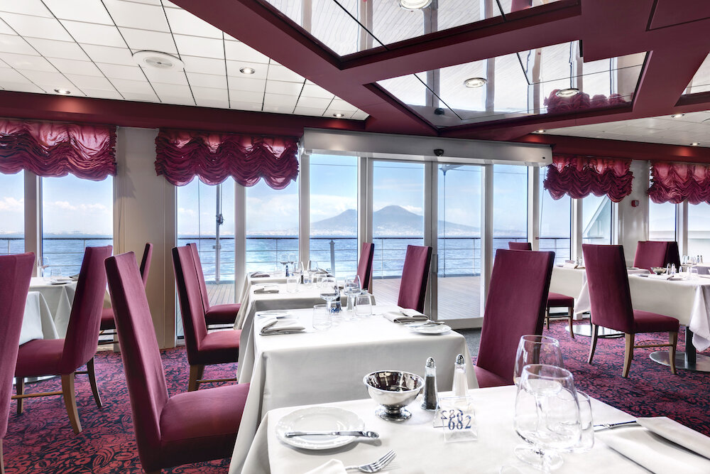 Restaurant mit Panoramafenstern und Blick auf den Vesuv in Neapel, gedeckten Tischen und karmesinroten Stühlen