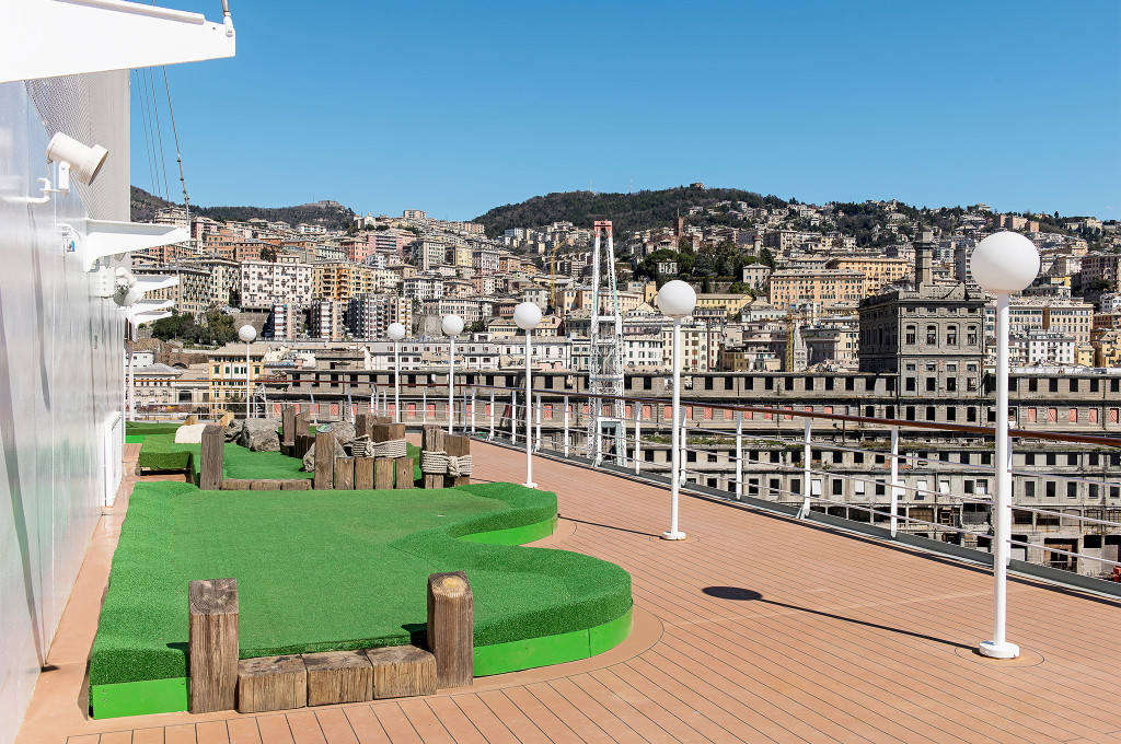 Minigolf-Anlage auf dem Sonnendeck der MSC Sinfonia mit Blick auf eine Hafenstadt und Hügel im Hintergrund