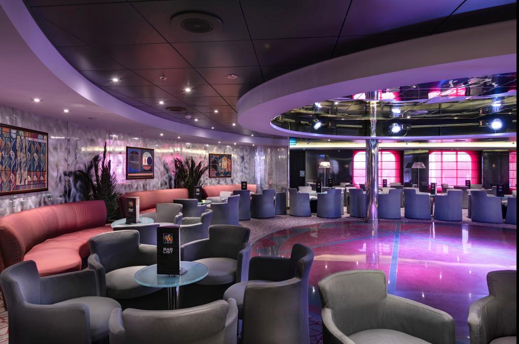 Großzügige Lounge der MSC Sinfonia mit grauen Sesseln, Tanzfläche, Kunstgemälden und violetter Stimmungsbeleuchtung