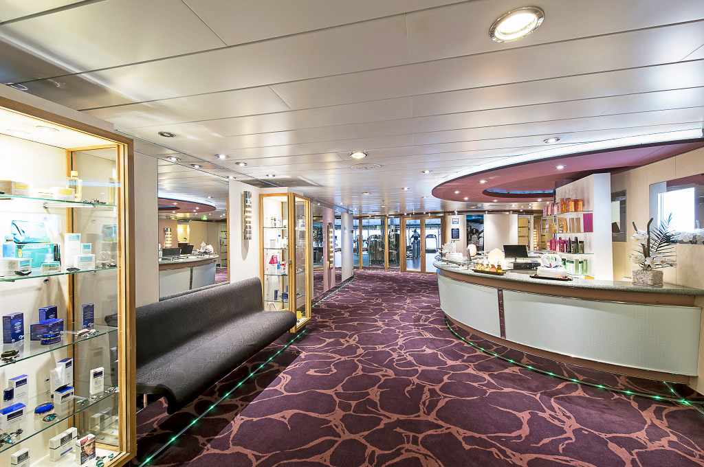Spa-Empfangsbereich der MSC Sinfonia mit Rezeptionstresen, Produktvitrinen und violettem Teppich