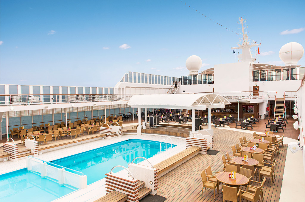 Pooldeck der MSC Sinfonia mit Außenpool, Liegestühlen, Außenbar und Rattanmöbeln unter blauem Himmel