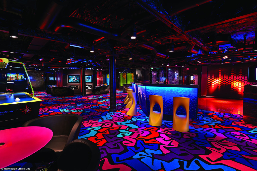 Teenager-Lounge mit Spielautomaten, bunter Beleuchtung, Barhockern und gemusterten Bodenteppichen an Bord.