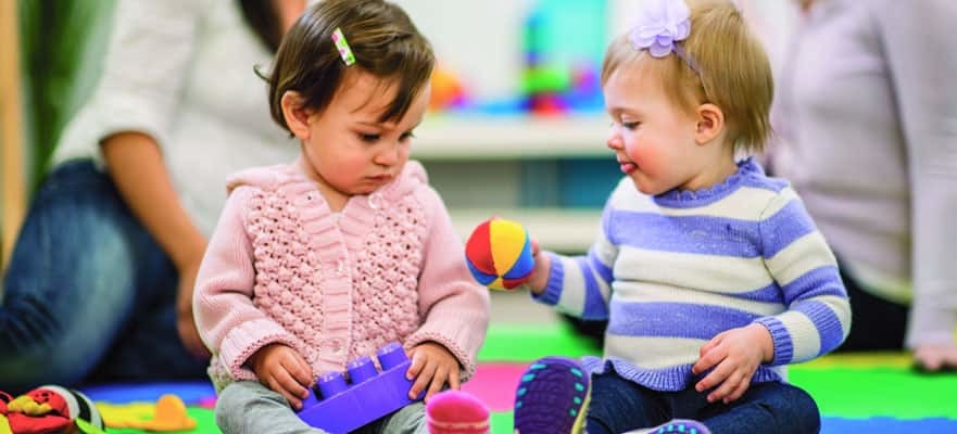 Zwei Kleinkinder spielen auf einer bunten Spielmatte mit Spielzeug im Kinderspielbereich eines Kreuzfahrtschiffes