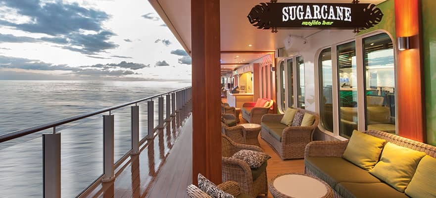 Gemütliche Außenlounge auf einem Hochseekreuzfahrtschiff mit Rattansofas und -sesseln, Kissen und Blick auf das abendliche Meer