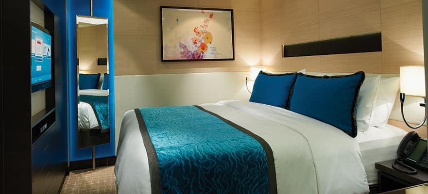 Moderne Innenkabine auf der Norwegian Getaway mit Doppelbett, türkisfarbenem Dekor, Wandspiegel und Flachbildschirm