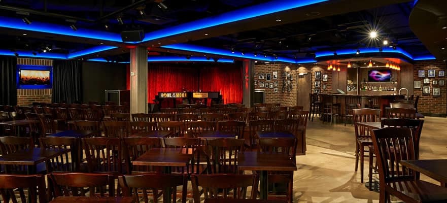 Showlounge auf der Norwegian Getaway mit Bühne, rotem Vorhang, Holztischen und Thekenbereich mit Backsteinwand