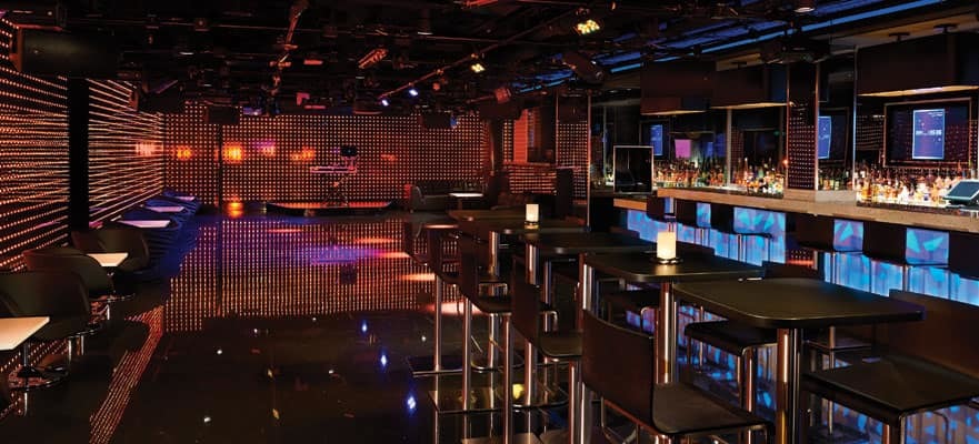 Moderner Nachtclub mit LED-Punktmatrix-Wänden, Tanzfläche, erhöhter DJ-Bühne und Bartresen auf einem Hochseekreuzfahrtschiff