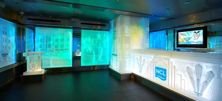 Beleuchteter Empfangsbereich auf der Norwegian Getaway mit Miami-Beach-thematischer Dekoration und beleuchtetem Tresen