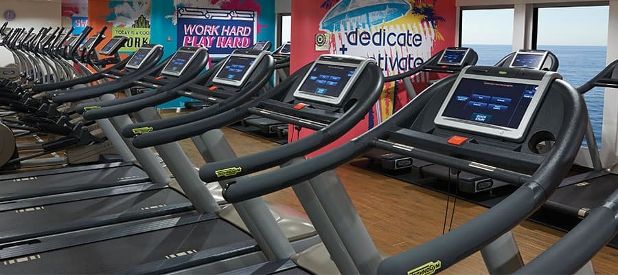 Fitnessraum mit Reihen moderner Laufbänder, bunter Motivationswandbemalung und Meerblick durch Panoramafenster auf einem Hochseekreuzfahrtschiff