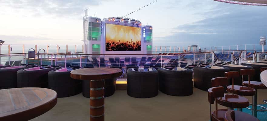 Außendeck mit großem LED-Bildschirm, runden Sitzinseln und Abendatmosphäre auf einem Kreuzfahrtschiff