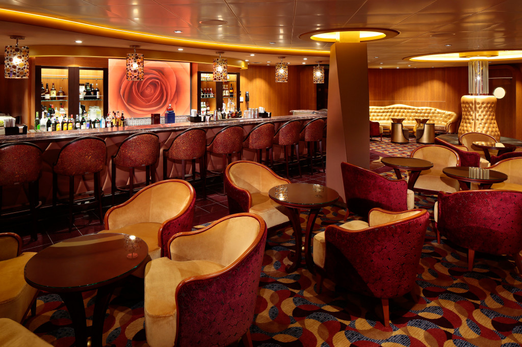 Stimmungsvolle Lounge-Bar mit Clubsesseln, Barhockern und warmer Beleuchtung an Bord eines Kreuzfahrtschiffs.