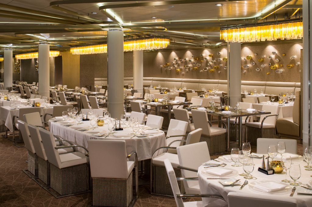 Großer eleganter Speisesaal mit eingedeckten Tischen, weißen Stühlen und goldenen Kristallleuchtern an Bord eines Kreuzfahrtschiffs.