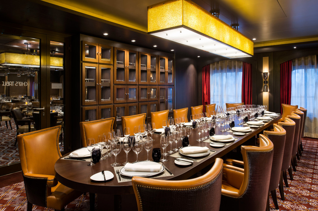 Langer eingedeckter Tisch mit Lederstühlen und goldener Deckenbeleuchtung für das Chef's Table Dinner an Bord eines Kreuzfahrtschiffs.