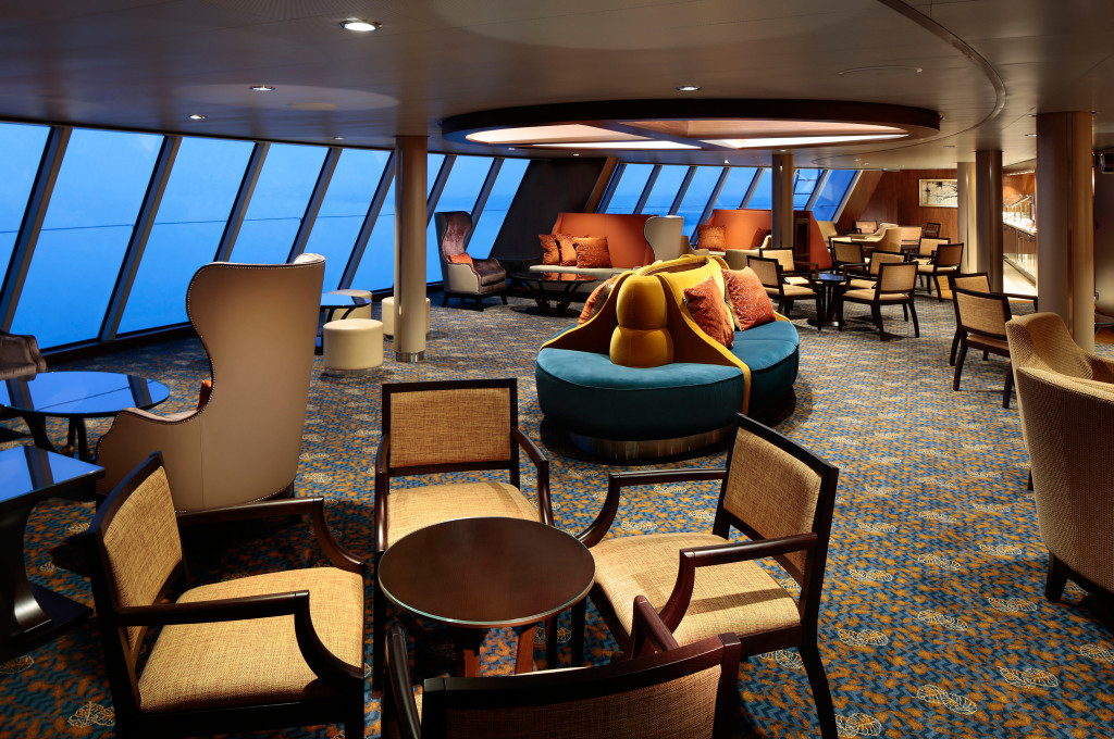 Panoramalounge mit bodentiefen Fenstern, Rundsofa und verschiedenen Sitzgruppen mit Meerblick an Bord eines Kreuzfahrtschiffs.