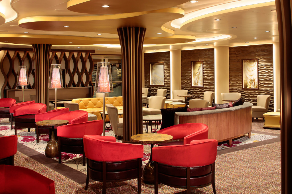 Elegante Lounge mit roten Clubsesseln, beigen Polstermöbeln und dekorativen Stehlampen an Bord eines Kreuzfahrtschiffs.