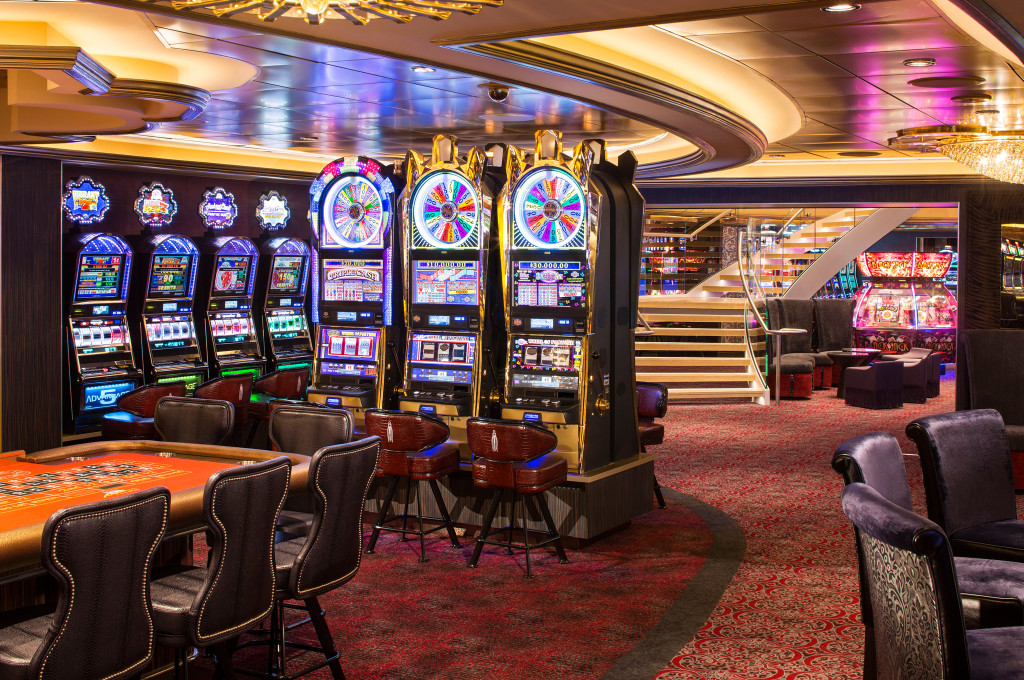 Bordcasino mit Reihen von Spielautomaten, Blackjack-Tisch und gedämpfter Beleuchtung an Bord eines Kreuzfahrtschiffs.