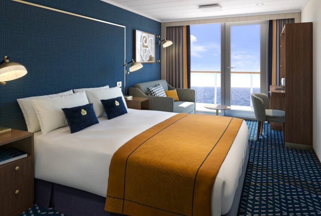 Balkonkabine auf der Queen Anne mit Doppelbett, marineblauen Akzenten, Sofa und Balkon mit Meerblick.