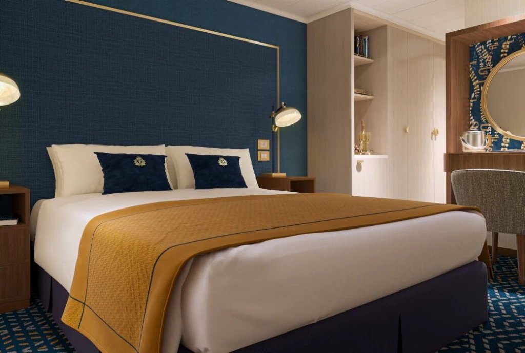 Innenkabine auf der Queen Anne mit Doppelbett, marineblauen Akzenten, Wandregalen und Kleiderschrank.