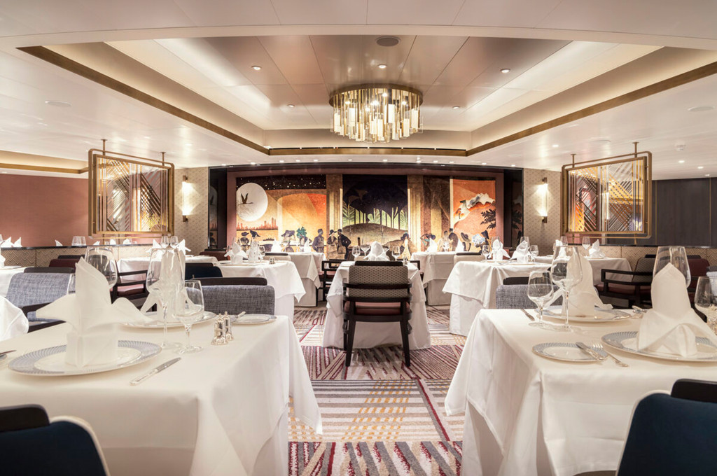 Britannia Club Restaurant auf der Queen Anne mit gedeckten Tischen, Kronleuchter und dekorativem Wandgemälde.