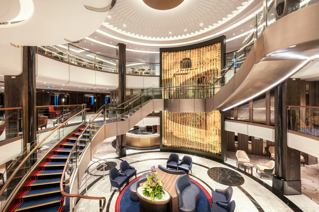 Grand Lobby der Queen Anne mit geschwungener Treppe, beleuchteter Lichtskulptur und Marmorboden.