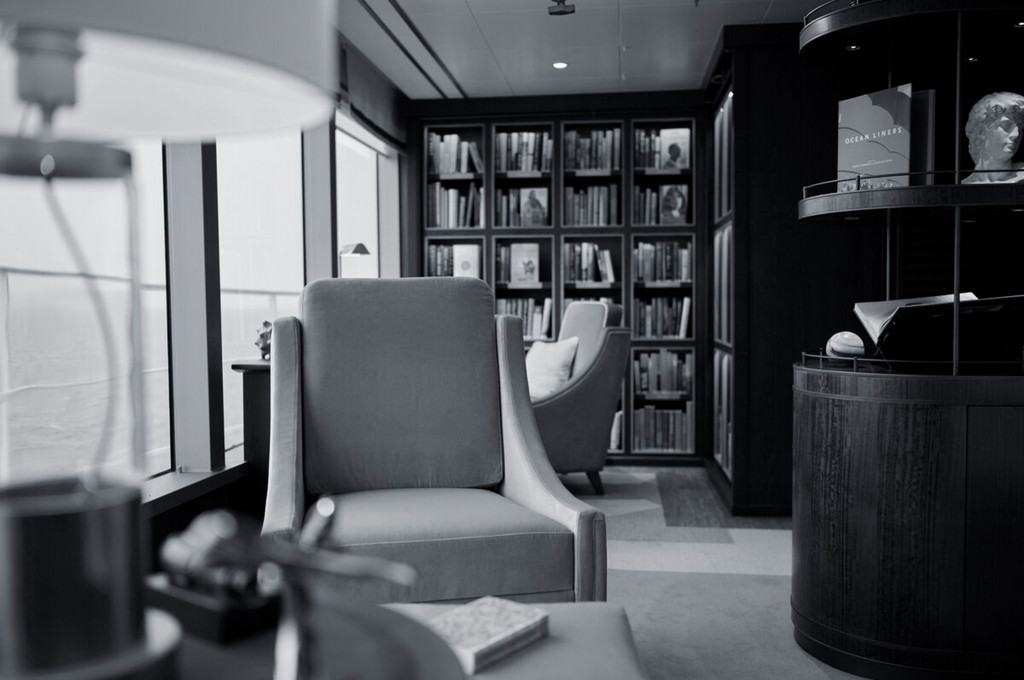 Bibliothekslounge eines Kreuzfahrtschiffes mit gefüllten Bücherregalen, Sesseln und Blick auf das Meer