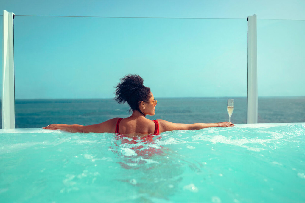 Frau entspannt im Whirlpool auf der Queen Anne mit Blick auf das offene Meer und einem Glas Sekt.