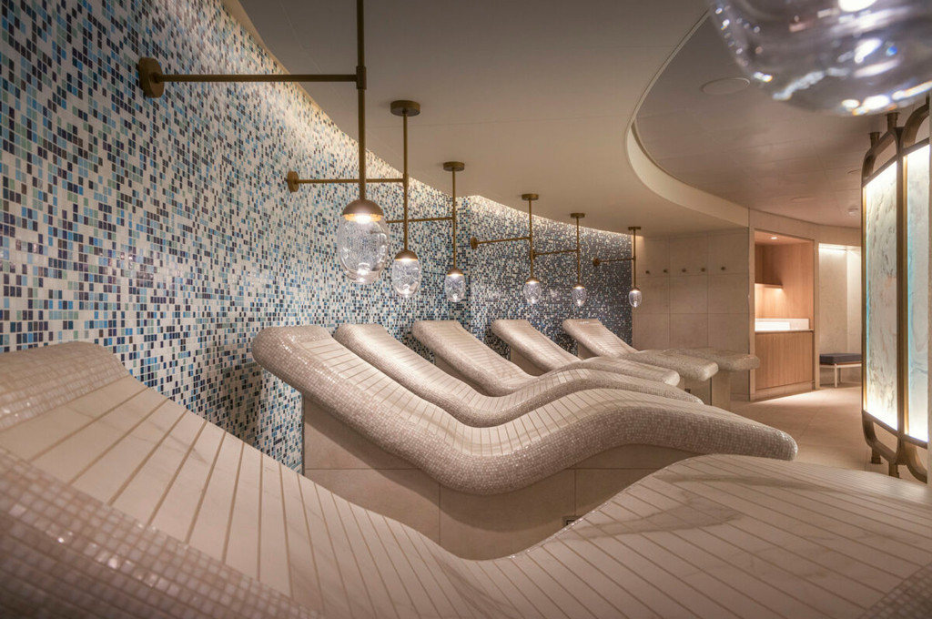 Wellnessbereich mit beheizten Mosaikliegen, blauer Mosaikwand und Messingpendelleuchten auf einem Kreuzfahrtschiff