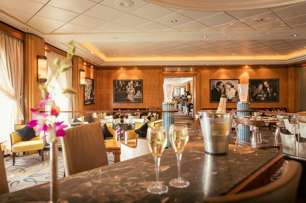 Champagnerbar der Queen Mary 2 mit Champagnergläsern, Filmfoto-Wanddekor, gelben Sesseln und warmer Holzverkleidung