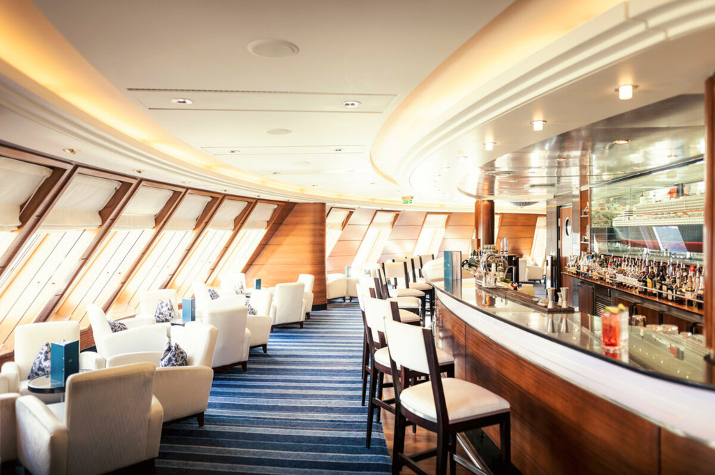 Commodore Club Bar der Queen Mary 2 mit charakteristischen Schrägpanoramafenstern, geschwungenem Tresen und weißen Sesseln